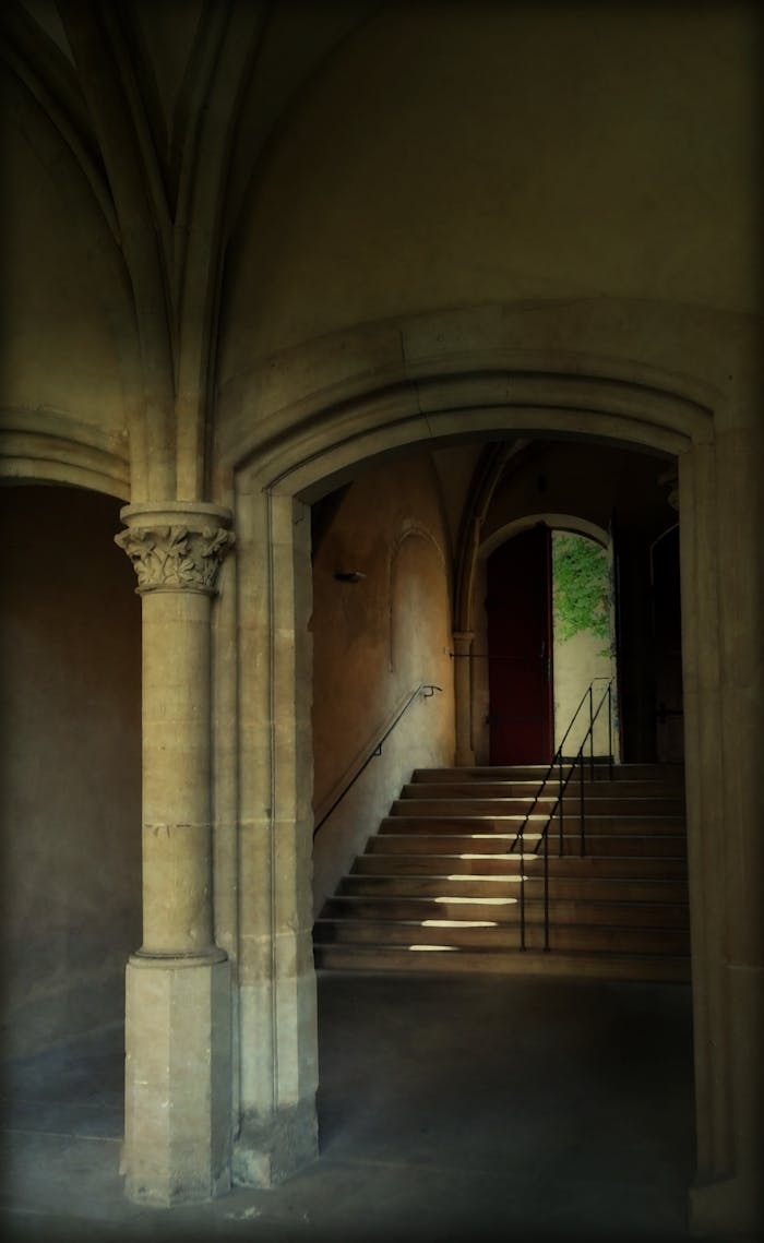 A historical stone cloister with arches and stairs creating dramatic shadows, evoking a sense of ancient architecture.