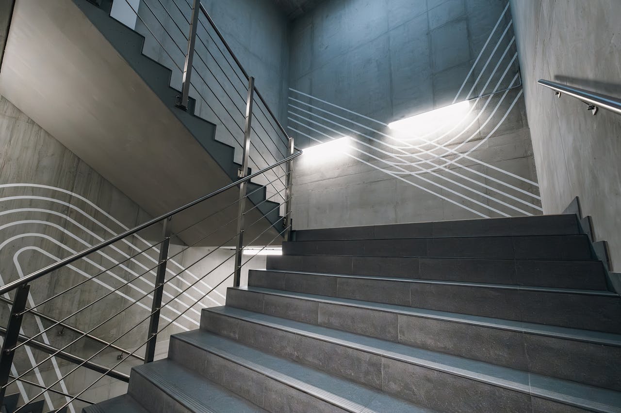 Abstract view of a modern concrete staircase featuring metal railings and geometric patterns.