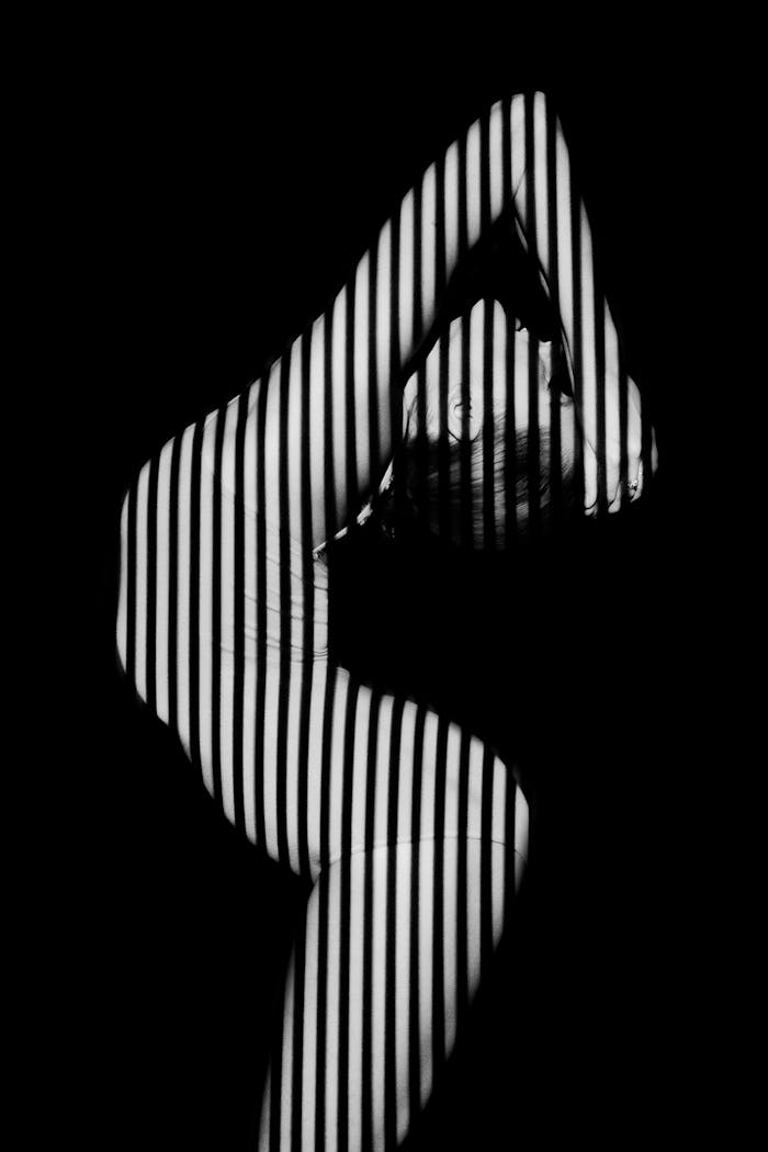 Artistic black and white photo of a contortionist with striped light effect, emphasizing contrast.